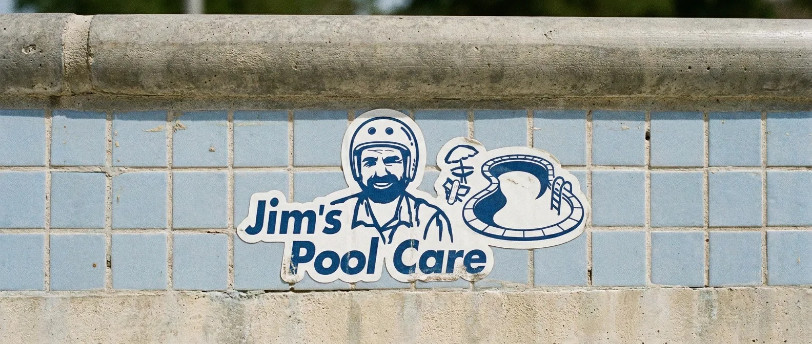 Jim's Pool Care sticker on the tiles of an empty pool, just under the coping